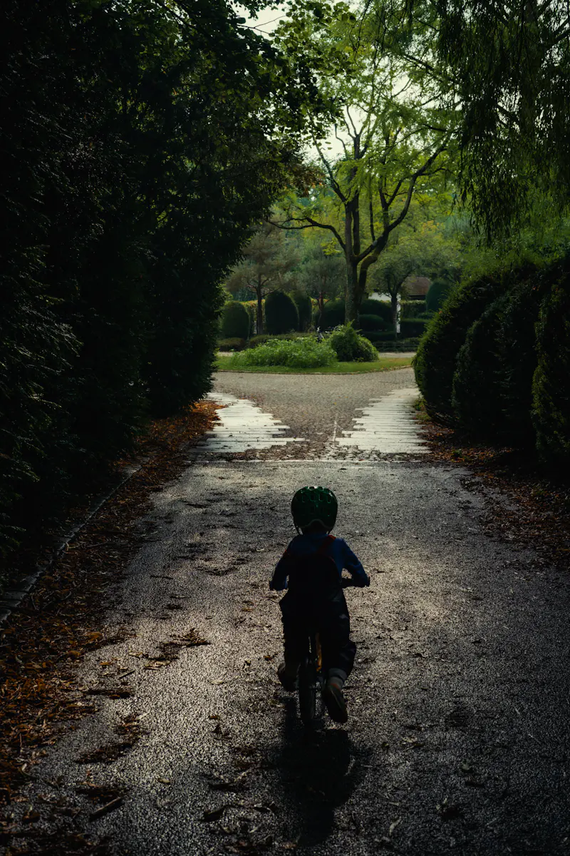 A child in a green helmet cycling down a wet lane between hedges